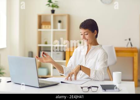 Smiling coach having online lesson with student or hosting webinar sitting at desk with laptop Stock Photo