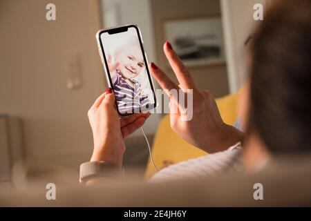 Mother showing peace sign to daughter on video chat at home Stock Photo