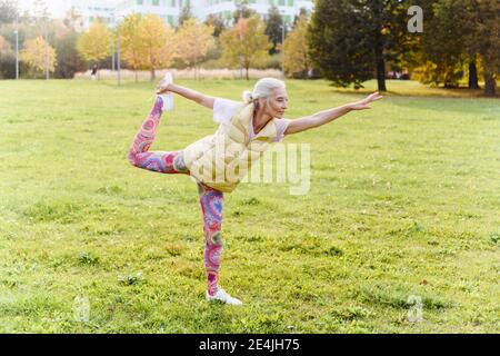 Mature woman doing yoga exercise on grass in public park Stock Photo