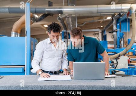 Two carpenters talking over documents in production hall Stock Photo
