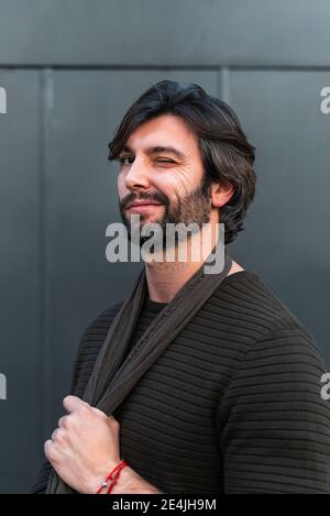 Portrait of smiling man wearing brown sweater and scarf in front of gray wall Stock Photo