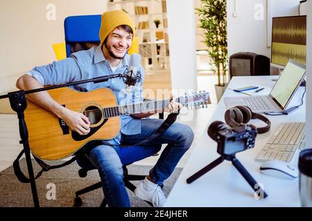 Happy musician playing guitar while recording on camera at recording studio Stock Photo