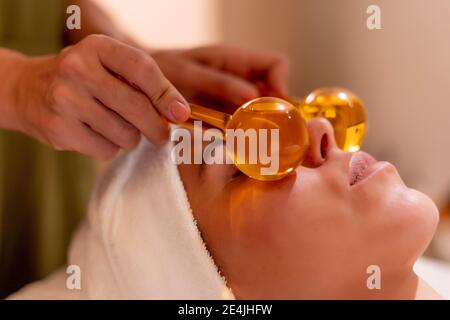Beautician holding glass globes on female customer's face during spa treatment