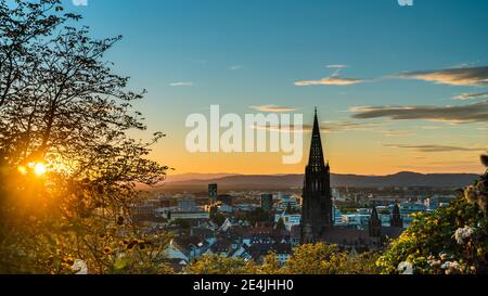 Germany, Freiburg im Breisgau, Magical orange sunset sky and sunrays behind skyline of the beautiful city and muenster Stock Photo