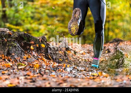Male trail runner running through mud in autumn forest at Kappelberg, Germany Stock Photo