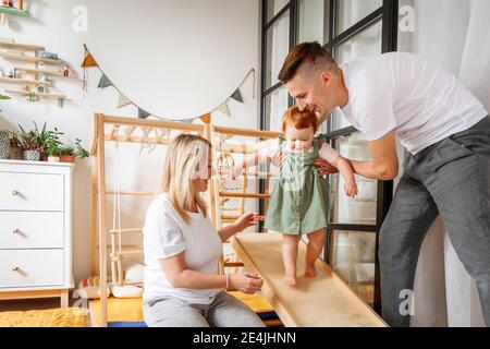 Parents assisting baby daughter walking at home Stock Photo