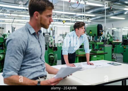Businessman looking away while standing with male colleague in industry Stock Photo