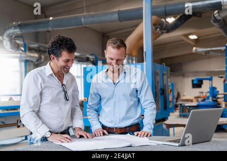 Two carpenters talking over documents in production hall Stock Photo