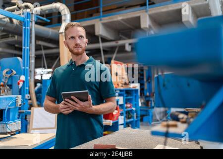 Portrait of carpenter standing in production hall with digital tablet in hands Stock Photo