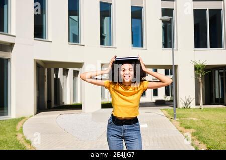 Smiling female student holding book while standing at university Stock Photo