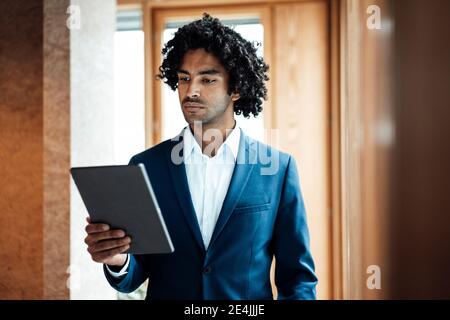 Confident young businessman with curly black hair using digital tablet at office Stock Photo