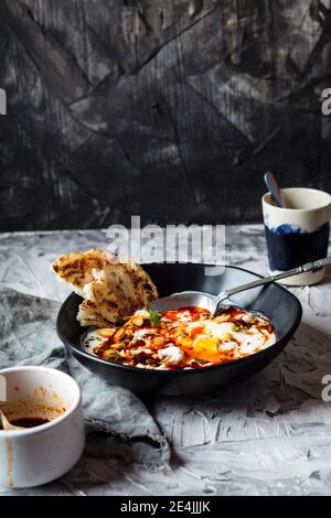 Breakfast of yogurt and spicy paprika butter on poached eggs in bowl by coffee cup on table Stock Photo