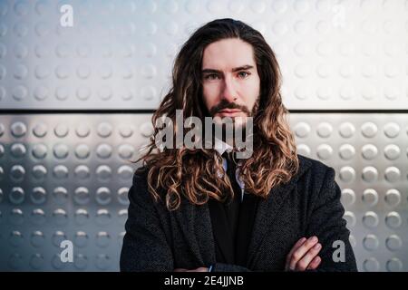 Young businessman with arms crossed staring while standing against silver wall Stock Photo