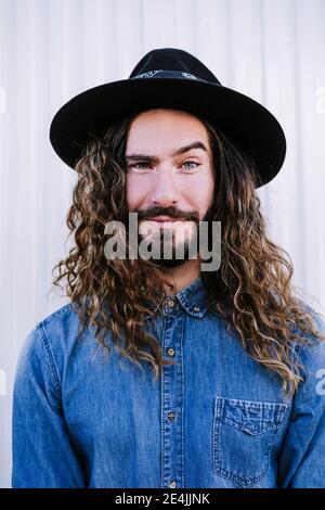 Handsome young man with raised eyebrow wearing hat against wall Stock Photo