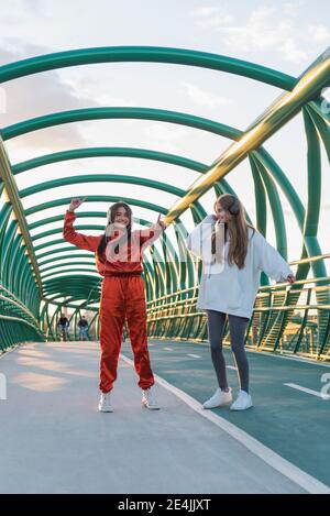 Carefree friends wearing headphones dancing while standing on bridge Stock Photo