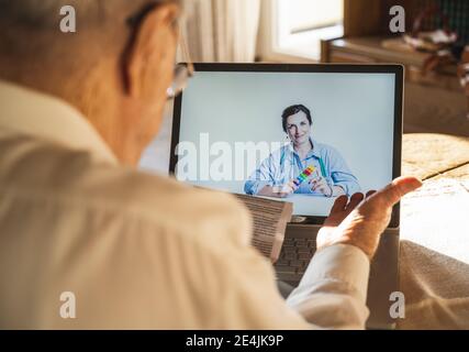 Male patient reading while female doctor consulting through video call on laptop at home Stock Photo