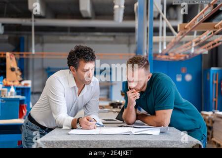 Two carpenters talking over documents in production hall Stock Photo