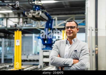 Businessman in suit with arms crossed standing in factory Stock Photo