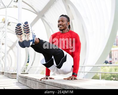 Smiling athlete doing handstand on bench at walkway Stock Photo