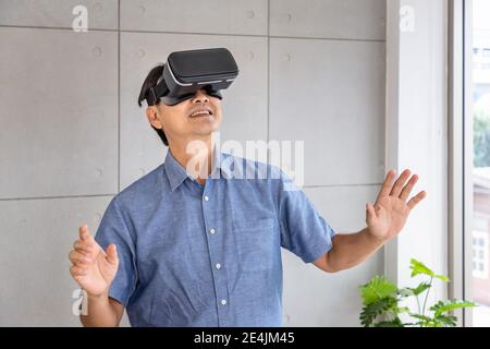 Senior retirement Asian man standing and wearing virtual reality glasses enjoy exciting experience Stock Photo