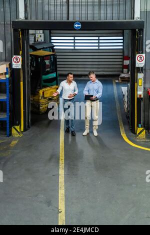 Male professionals discussing business strategy while walking in factory Stock Photo