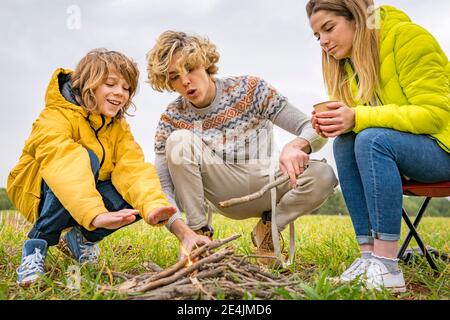 Three siblings starting campfire in grassy field Stock Photo