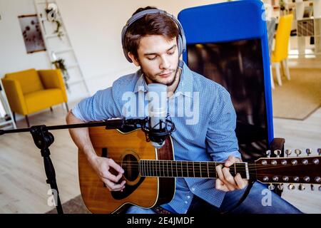 Professional with headphones and microphone playing guitar while sitting at recording studio Stock Photo