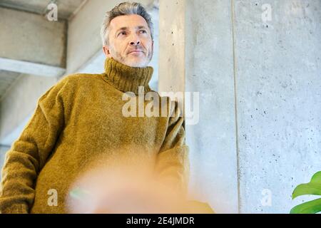Thoughtful mature man looking away while leaning on pillar at office Stock Photo