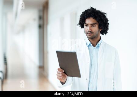 Confident young male doctor using digital tablet in corridor at hospital Stock Photo