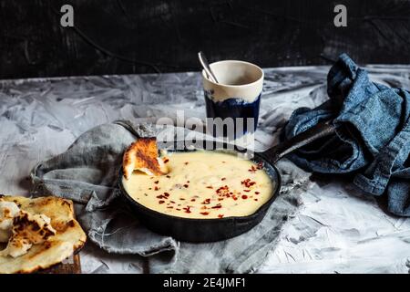 Kuymak in cooking pan by coffee cup on table Stock Photo