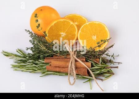 Fresh oranges with cinnamon sticks tied together with rosemary and thyme, white background Stock Photo