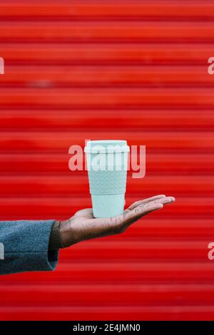 Man holding disposable cup in hand against red wall Stock Photo