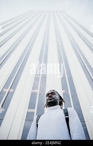 Young businessman thinking while standing against skyscraper in city Stock Photo