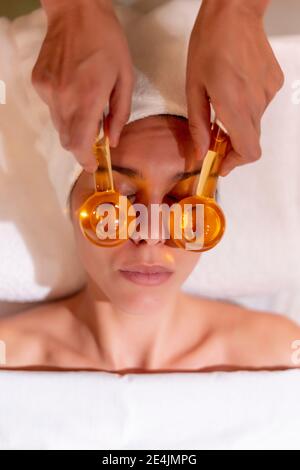 Female beautician holding glass globes on customer's face at health spa