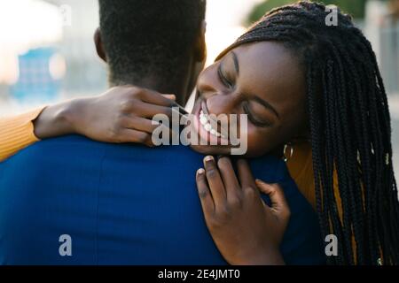 Smiling teenage girl with eyes closed hugging boyfriend outdoors Stock Photo