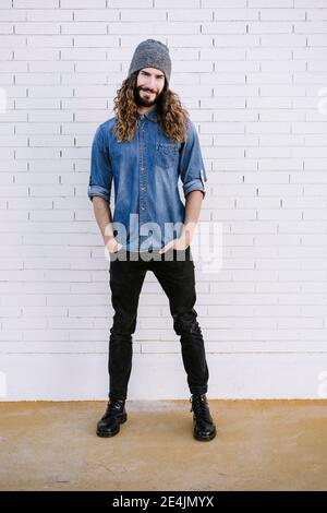 Smiling stylish man with hands in pockets against brick wall Stock Photo
