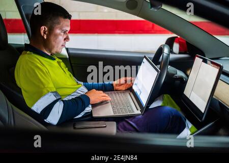 Male technician working on laptop for programming in electric car Stock Photo