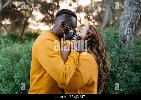Couple wearing protective face mask kissing while standing at forest Stock Photo