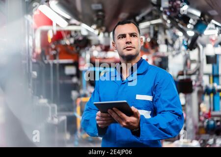 Confident male engineer holding digital tablet while looking away in factory Stock Photo