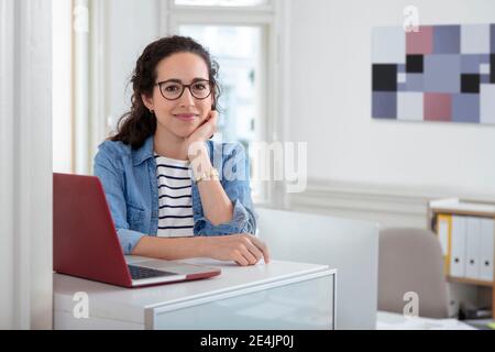 Female professional sitting by laptop at desk in office Stock Photo