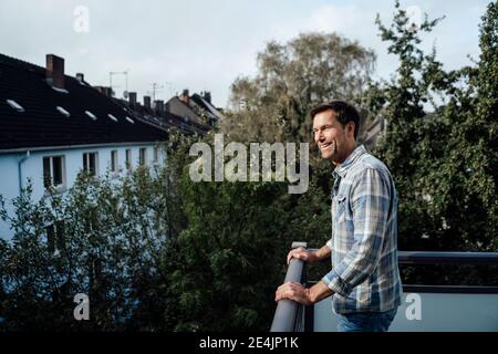 Happy mature man looking away while standing in balcony Stock Photo