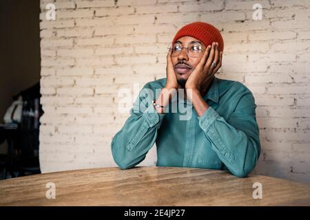 Thoughtful man leaning on table against white brick wall Stock Photo