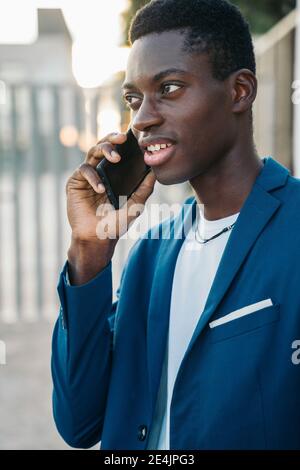 Young businessman in blazer talking on mobile phone call outdoors Stock Photo