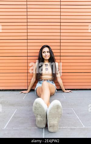 Young woman relaxing while sitting against wall Stock Photo