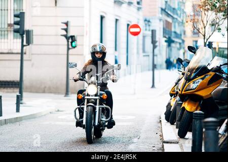 Biker woman in helmet wearing leather jacket while looking away in city Stock Photo