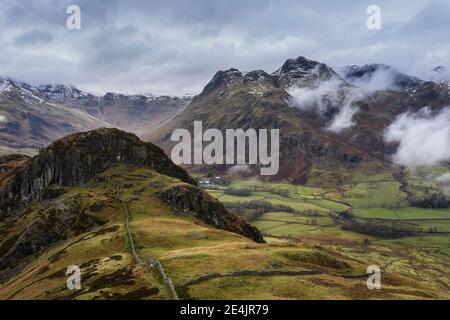 Epic flying drone landscape image of Langdale pikes and valley in Winter with low level clouds and mist swirling around Stock Photo