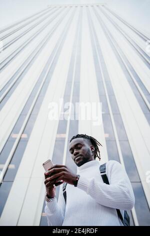 Young creative professional using smartphone against skyscraper in city Stock Photo
