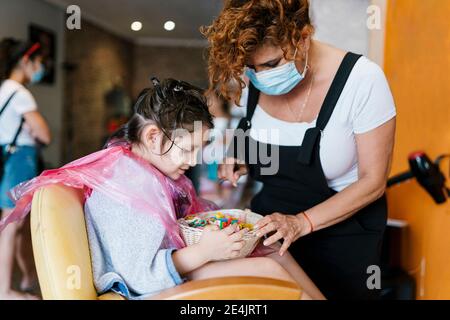 Hairdresser and girl searching in basket with hair clips at barber shop during coronavirus Stock Photo