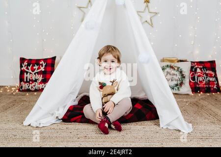 Cute baby girl smiling while sitting in tent during Christmas at home Stock Photo