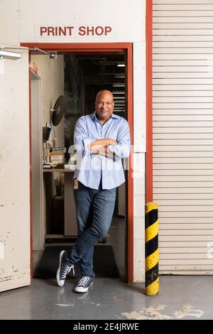 Cheerful employee with hands behind head laughing while sitting in print shop Stock Photo